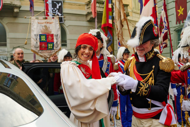 Ivrea, Italy - March 02, 2025: a young woman with the mugnaia (Miller's Daughter) costume at Ivrea Carnival. She is the symbol of freedom and the heroine of the festival since her appearance in 1858. She is parading though the city accompained by the General. According to legend, the brave maiden liberated the people from tyranny by killing the Marquis of Monferrato, who starved the city and forced young brides to the ius primae noctis. The miller first seduced the nobleman, then she rebelled on the night of the encounter, cutting off his head with his own sword and initiating the popular uprising.
