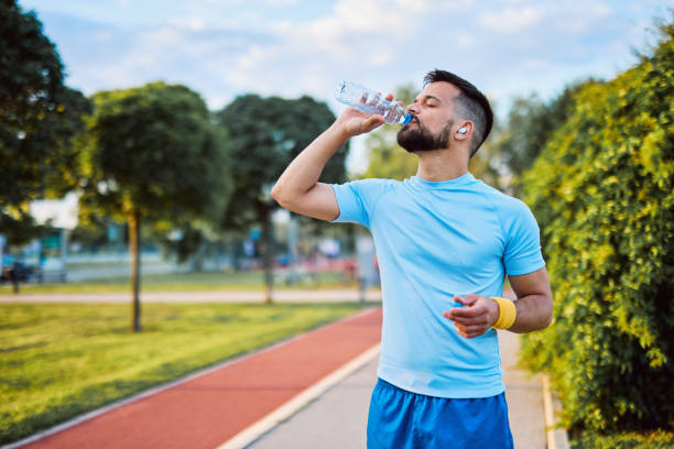 vận động viên uống nước sau khi chạy trong công viên - tai nghe chống nước hình ảnh sẵn có, bức ảnh & hình ảnh trả phí bản quyền một lần