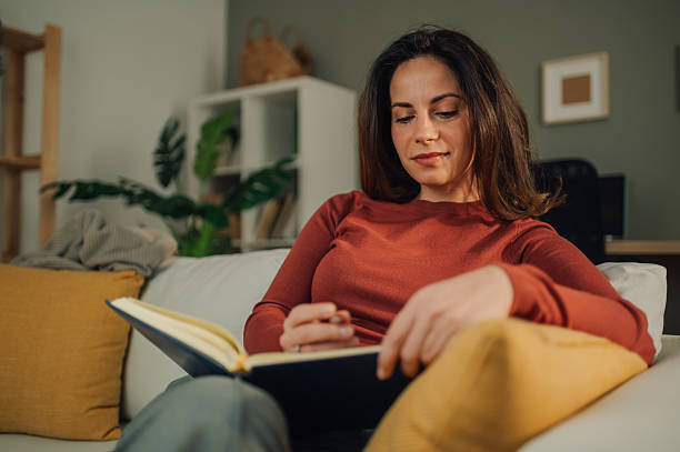 istock Woman relaxing on sofa reading and taking notes in notebook at home 2205435807