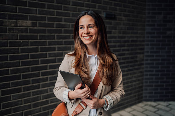 istock Smiling young businesswoman holding digital tablet by brick wall 2205436490