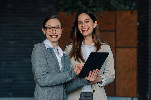 istock Two smiling businesswomen using digital tablet outdoors 2205436552