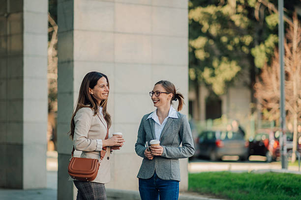 istock Two businesswomen talking and smiling outdoors while holding coffee 2205436560