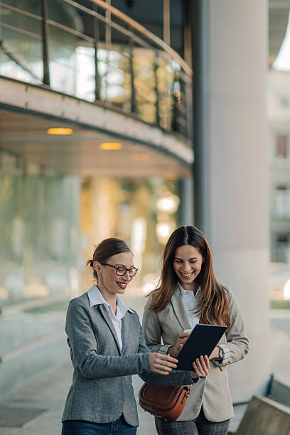 istock Two businesswomen smiling and using a digital tablet outside office building 2205436576