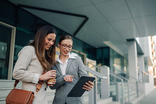 istock Businesswomen using digital tablet and drinking coffee outside office building 2205436586
