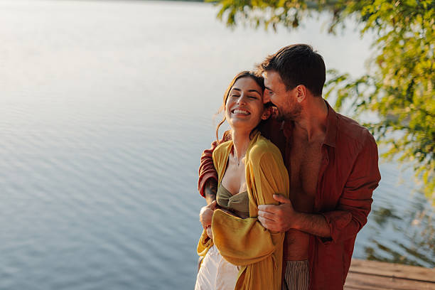 istock Happy couple embracing on pier at sunset by lake 2205437671