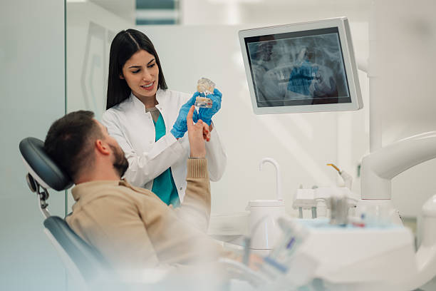 istock Dentist showing teeth x-ray to patient explaining treatment with jaw model 2205440982