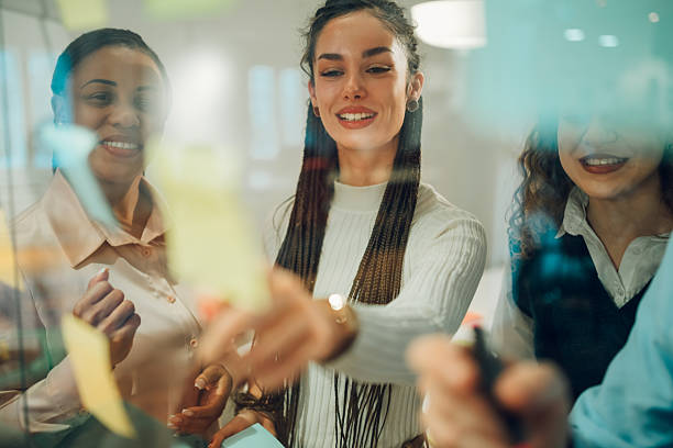 istock Businesswomen planning strategy using adhesive notes on glass wall in office 2205441262