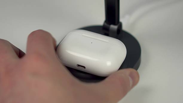 istock Wireless headphones are placed on a magnetic charging station. Wireless charging on a white table. Closeup. 2205442191
