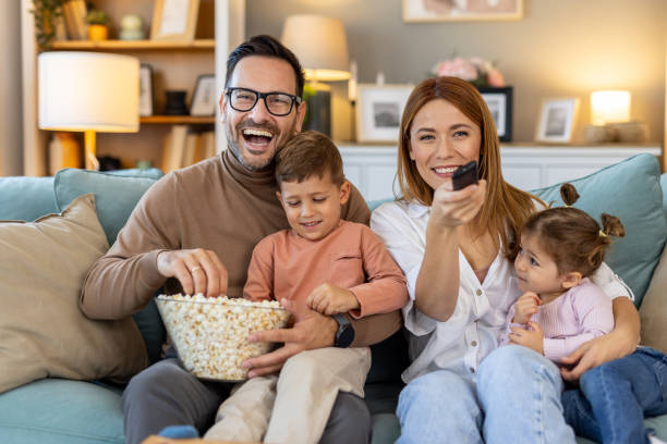 istock Parents and kids gleefully watching movie with shared popcorn bowl. 2205446515