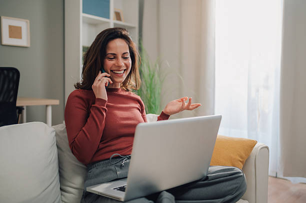 istock Smiling woman using laptop and talking on smartphone while working from home 2205454355
