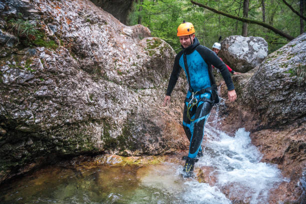 Geared up in neoprene suits and safety helmets, Caucasisan male and diverse friends enjoy outdoor fun as they walk through canyons during a thrilling canyoning expedition.