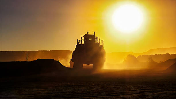 silhouette of truck mining equipment and front loader at a diamond mine ,outdoors sunset with orange sky and sun reflection rays late in the day
