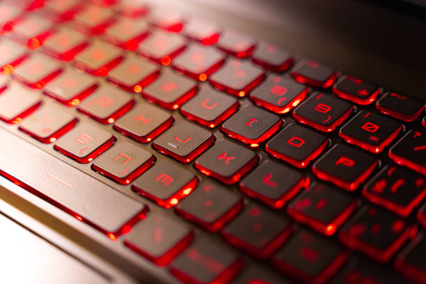Close-up of a laptop keyboard with illuminated red backlighting, showcasing the keys and their reflections.