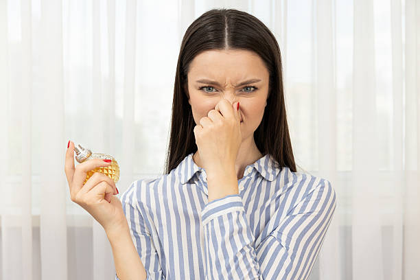 Dissatisfied woman with perfume bottle  in hand on light background