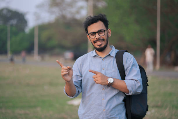 istock Cheerful Young Man with Backpack Pointing Outdoors 2205464526