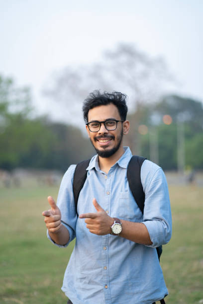 istock Cheerful Young Man with Backpack Pointing Outdoors 2205464561