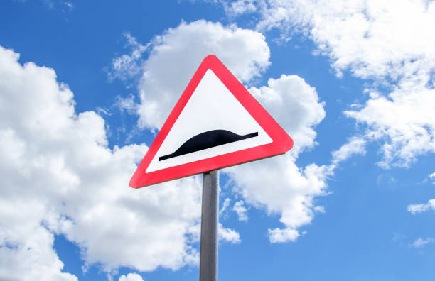 Road sign indicating a speed bump on a cobblestone pedestrian path with spring greenery and blooming chestnut trees in the background. Urban traffic safety symbol in a scenic park area.