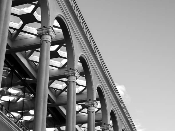 Abstract geometric pattern from bottom view of vintage design construction building, glass ceiling with concrete poles background on sky background, in black and white, monochrome.