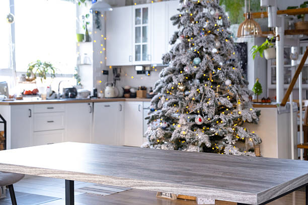 istock Grey Wooden empty table to demonstrate product with space for text with upholstered chairs in white kitchen, modern interior with Christmas tree and fairy lights. New Year, Christmas mood, cozy home. 2205470842