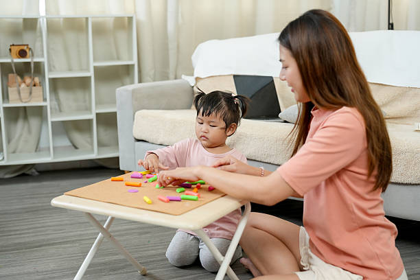 istock Single mother guiding young daughter through a creative learning activity at home. Sitting together at small table using colorful foam pieces for hands-on early education. Warm and cozy home setting. 2205473083