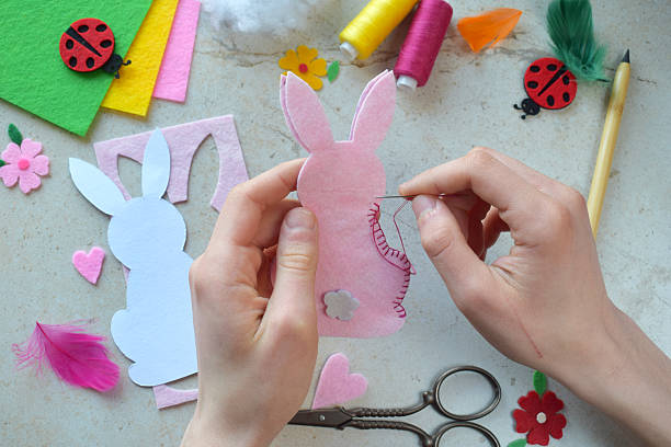 istock Hand Sewing Pink Felt Bunny with Needle and Thread for Easter DIY Craft Project. Creative Handmade Rabbit Decoration with Colorful Accessories, Paper Template, and Scissors on Light Background 2205474096
