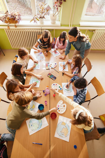 Above view of students having an art class with elementary teacher at school.