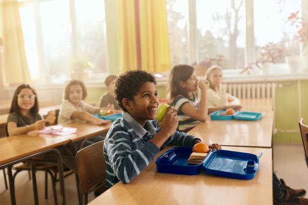 istock Happy black boy having fruit for snack during a break in the classroom. 2205474233