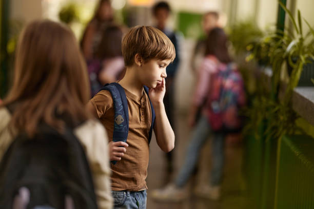 istock Displeased schoolboy standing alone in a hallway of elementary school. 2205474323