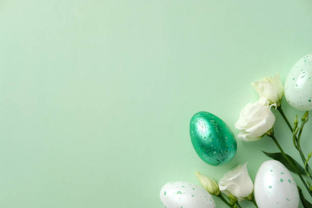 istock Green and white speckled Easter eggs paired with delicate white flowers on a pastel green background 2205476937