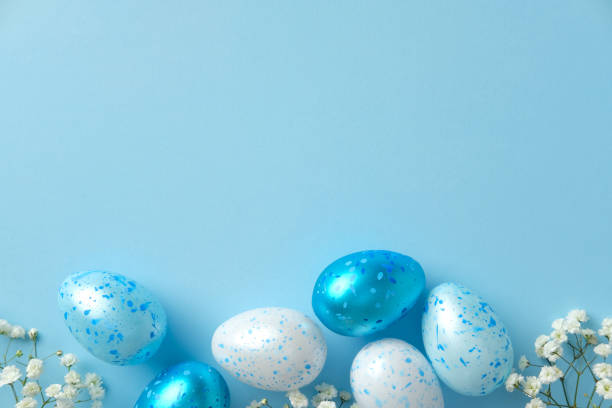 istock Blue and white speckled Easter eggs with white flowers on a pastel blue background. Flat lay, top view. 2205477159