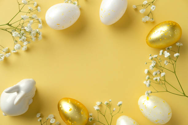 istock Festive Easter flat lay. White and gold speckled eggs, delicate flowers, and a ceramic bunny on a vibrant yellow background 2205477191