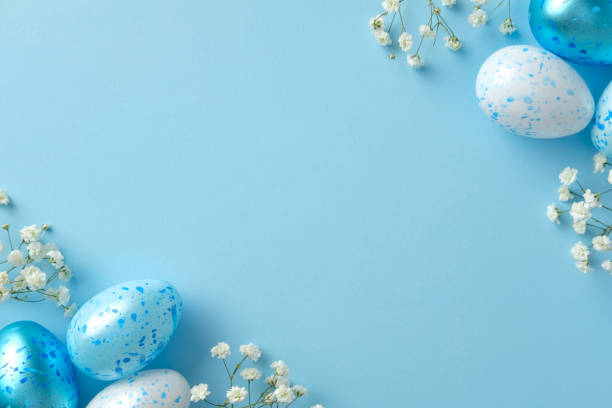 istock Pastel Easter scene with speckled blue and white eggs and small white flowers on a light blue background. 2205477256