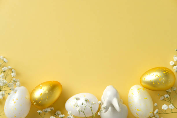 istock Stylish Easter flat lay. White and gold speckled eggs, a ceramic bunny figurine, and delicate white flowers on a vibrant yellow backdrop 2205477284