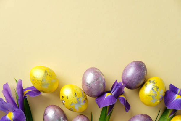 istock Easter flat lay composition. Vibrant yellow and purple metallic eggs, with purple irises, set on a light yellow background. 2205477450