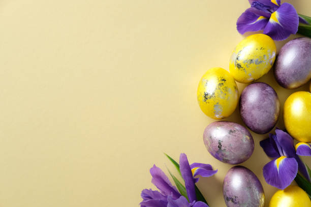 istock Elegant Easter flat lay composition with golden and purple eggs, vibrant purple irises on a pastel yellow background. 2205477494