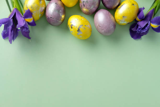 istock Happy Easter greeting card template. Flat lay composition with purple and golden Easter eggs, and iris flowers on pastel green background. 2205477603