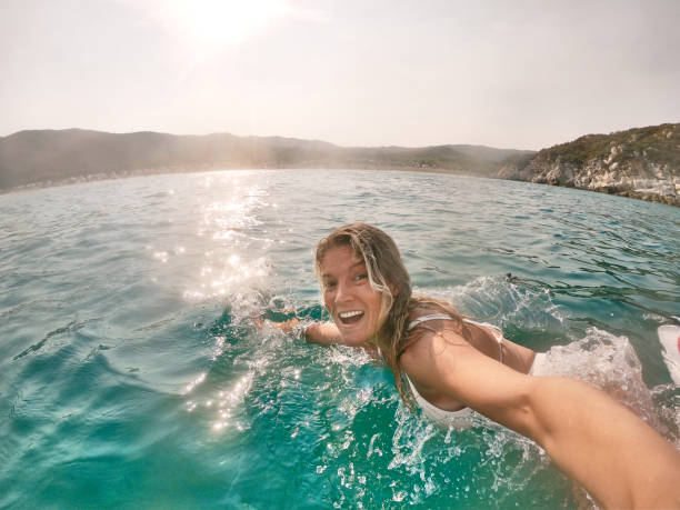 Happy young adult female taking a selfie. She is swimming during a beautiful sunset.