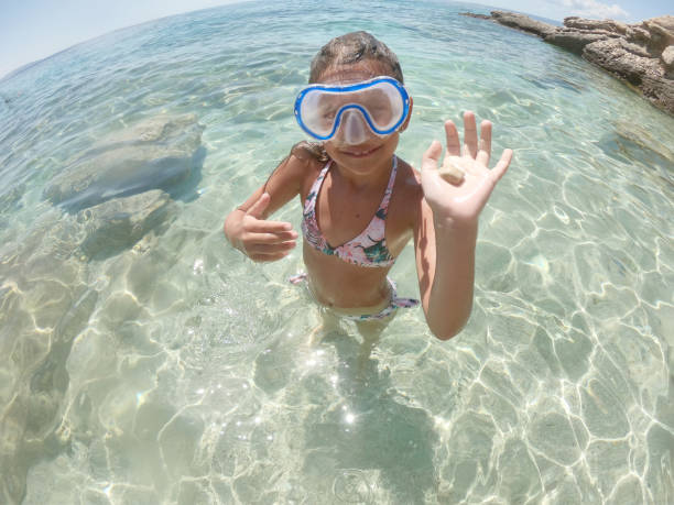 Young caucasian girl snorkeling and finding seashells. She is swimming and diving in clear turquoise colored sea.
