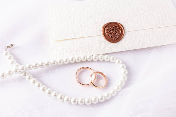 istock Wedding Arrangement with Wedding Rings, Pearl Beads, Envelope Invitation with Stamp on White Satin Background. top view. wedding layout, design. 2205482368