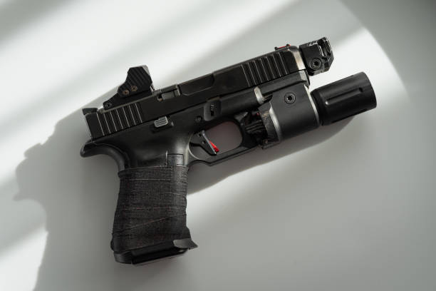 istock Civilian tactical weapon, pistol with flashlight and red dot sight on the white table. 2205482428