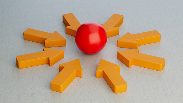 3D render showing multiple orange arrows pointing towards a central red sphere on a grey background. Represents concepts like focus, attention, attraction, converging ideas, teamwork, collaboration, a central theme, or gathering around a key point.