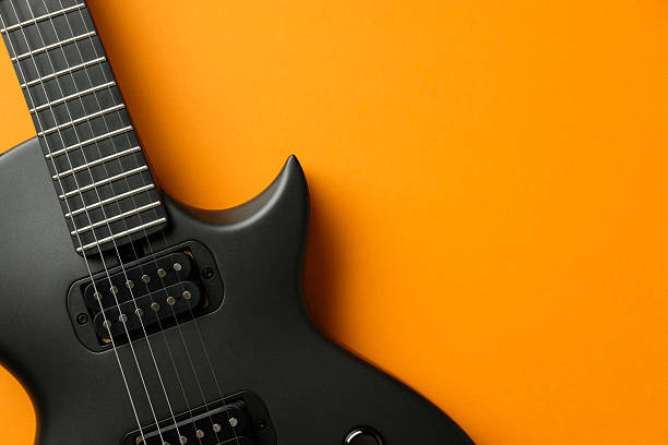Stylish black electric guitar isolated on a vibrant orange background.