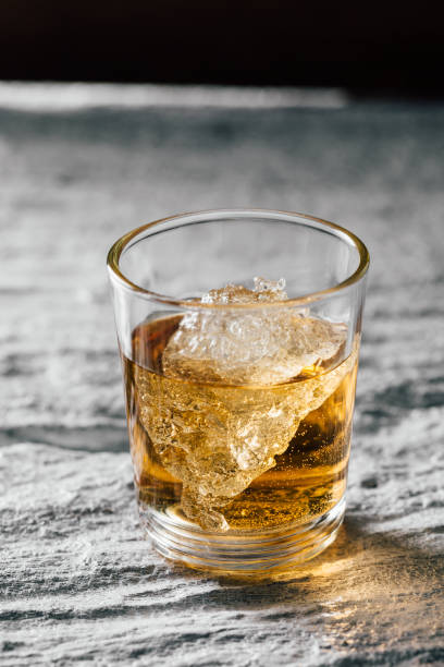 istock Glass of Whiskey with Ice Cube on Textured Surface Under Soft Natural Light 2205495049