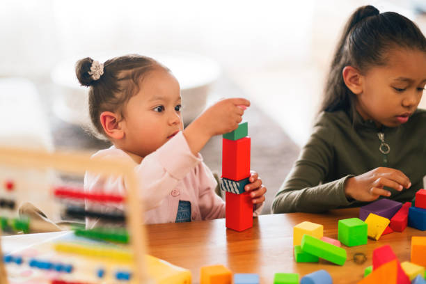 istock Playing, education and children with building blocks in home for development, fun and growth. Game, puzzle and girl kids with geometric activity for skills and cognitive learning with toys in house 2205496140