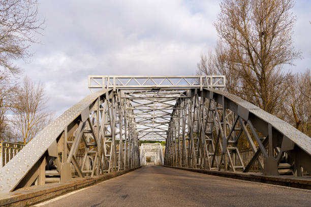 Metal truss bridge structure rising in a winter landscape, surrounded by bare trees and highlighting industrial design and engineering against a backdrop of a cloudy sky