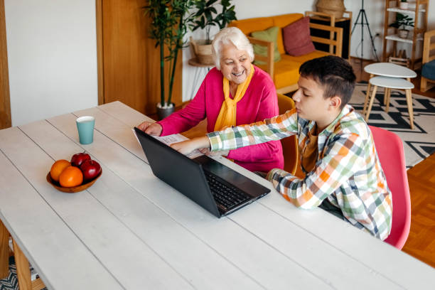 istock Teenager boy spending time with grandmother at home assisting her to pay bill using computer laptop at home 2205500992