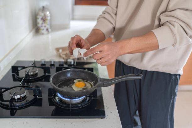 istock Man Breaking Eggs Into Hot Frying Pan 2205505037