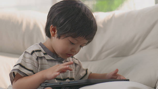 istock Happy Asian boy watching cartoon on tablet, e-learning at living room. 4k. 2205505526