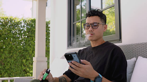 istock Asian man using smartphone and smoking electric cigarette. 4K 2205506867