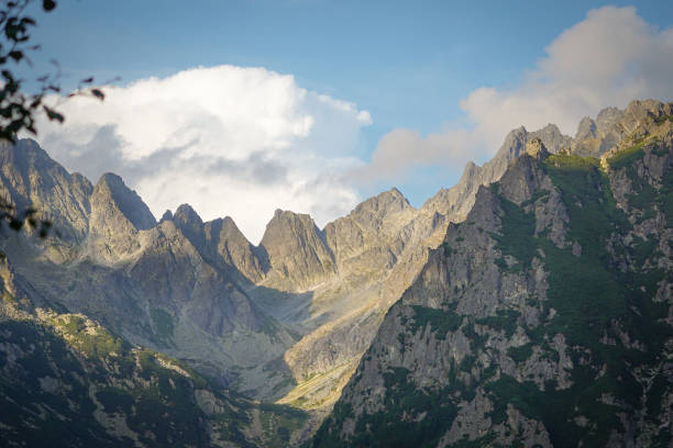 Sunlit Tatra Mountain peaks with low clouds, sharp shadows and blue sky in the background, High Tatra mountains, Slovakia